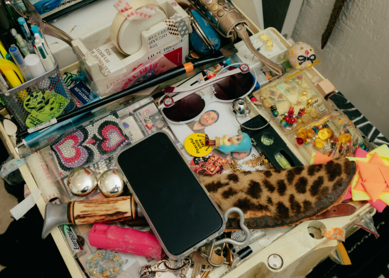 Cluttered tabletop with assorted items including a smartphone, sunglasses, pens, sewing supplies, buttons, and animal print pouch.