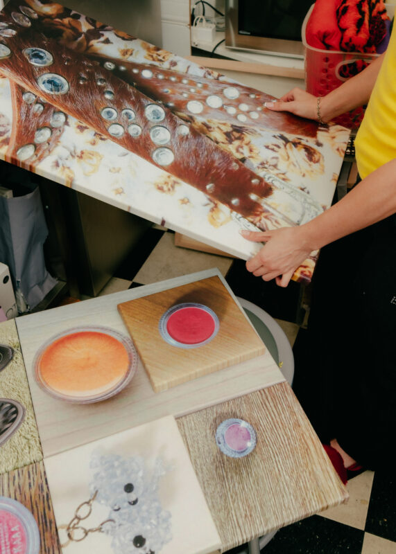A person holds a canvas with abstract art while other painted canvases featuring round objects rest on a table nearby.