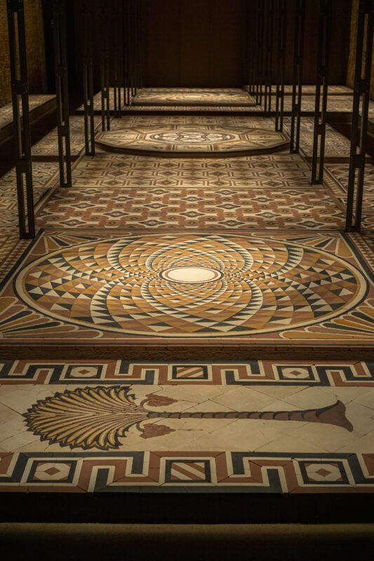 Intricate geometric and palm tree patterned floor mosaics arranged in rows within a dimly lit room.