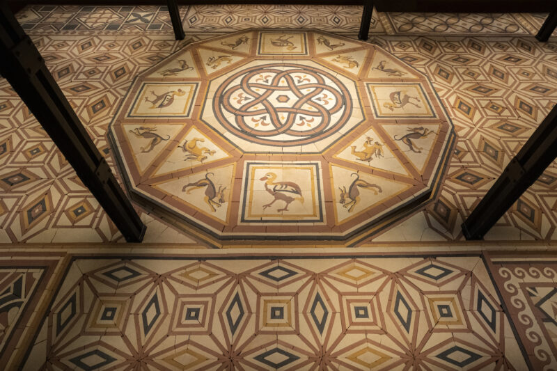 Ornate tiled floor featuring an octagonal central medallion decorated with bird and animal figures, surrounded by geometric patterns.
