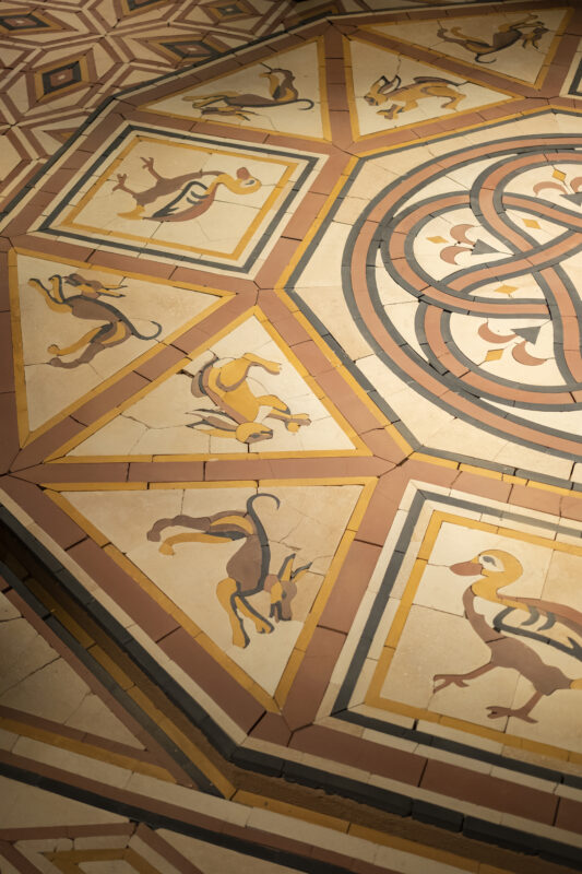 Geometric floor tiles featuring stylized images of birds and hares in a repeating triangular and circular pattern.