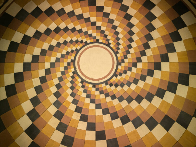 A circular floor pattern of orange, black, and cream tiles arranged in a radiating spiral around a solid center circle.